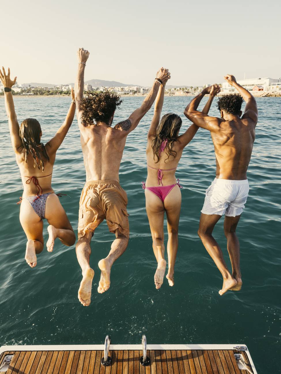 Group of friends holding hands and jumping into the ocean from a boat, enjoying summer vacation